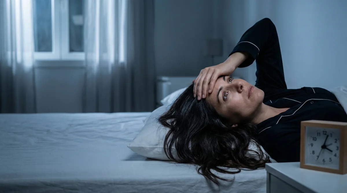 Woman lying awake in bed at night looking stressed with hair spread on pillow